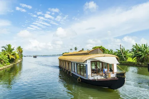 A traditional houseboat glides through a tranquil, palm-fringed canal in the beautiful backwaters of Alleppey, Kerala