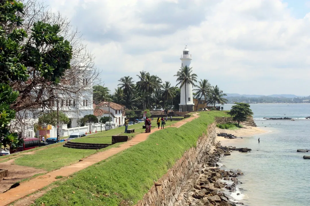 Tourists walk along the grassy ramparts of the colonial-era Galle Fort towards the iconic white lighthouse on the Sri Lankan coast