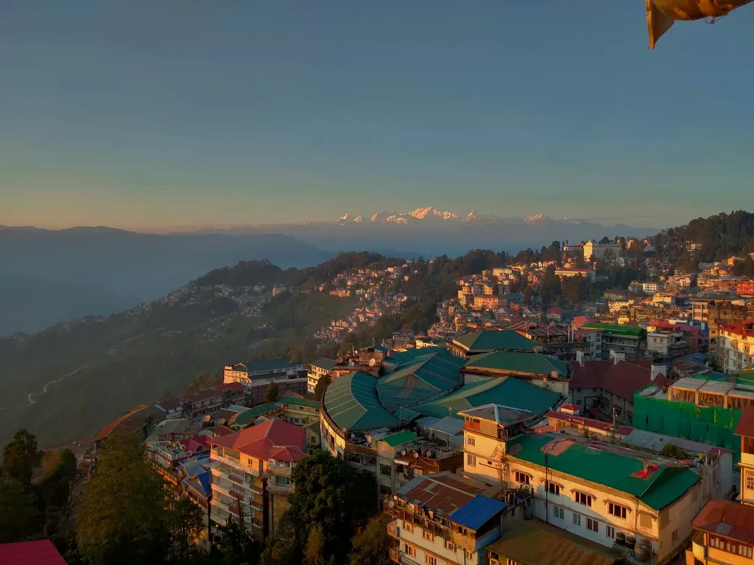 The town of Darjeeling awakens in the golden light of sunrise, with the majestic, snow-capped Kanchenjunga range visible on the horizon