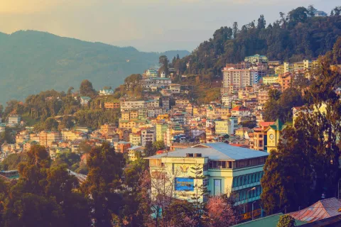 The colorful cityscape of Gangtok, with buildings clustered on the lush green Himalayan hills, glowing in warm sunset light