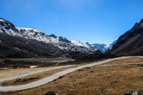 A winding road through the barren, high-altitude valley of Zero Point, Sikkim, surrounded by rugged, snow-dusted mountains