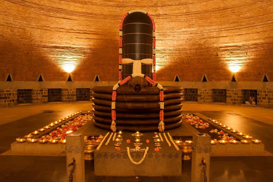 The serene Dhyanalinga lingam, adorned with garlands and surrounded by lit oil lamps, inside the domed brick meditation hall