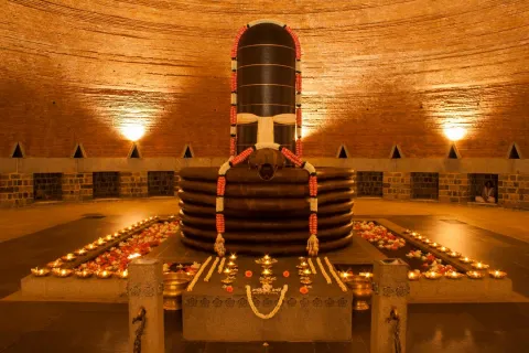 The serene Dhyanalinga lingam, adorned with garlands and surrounded by lit oil lamps, inside the domed brick meditation hall