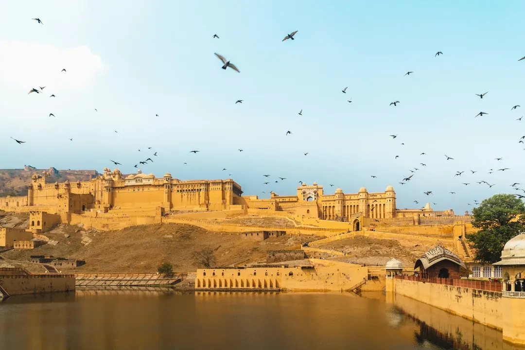 Birds fly over the sprawling, sand-colored Amer Fort as it sits on a hilltop overlooking Maota Lake in Jaipurs