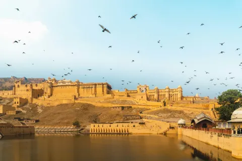 Birds fly over the sprawling, sand-colored Amer Fort as it sits on a hilltop overlooking Maota Lake in Jaipurs