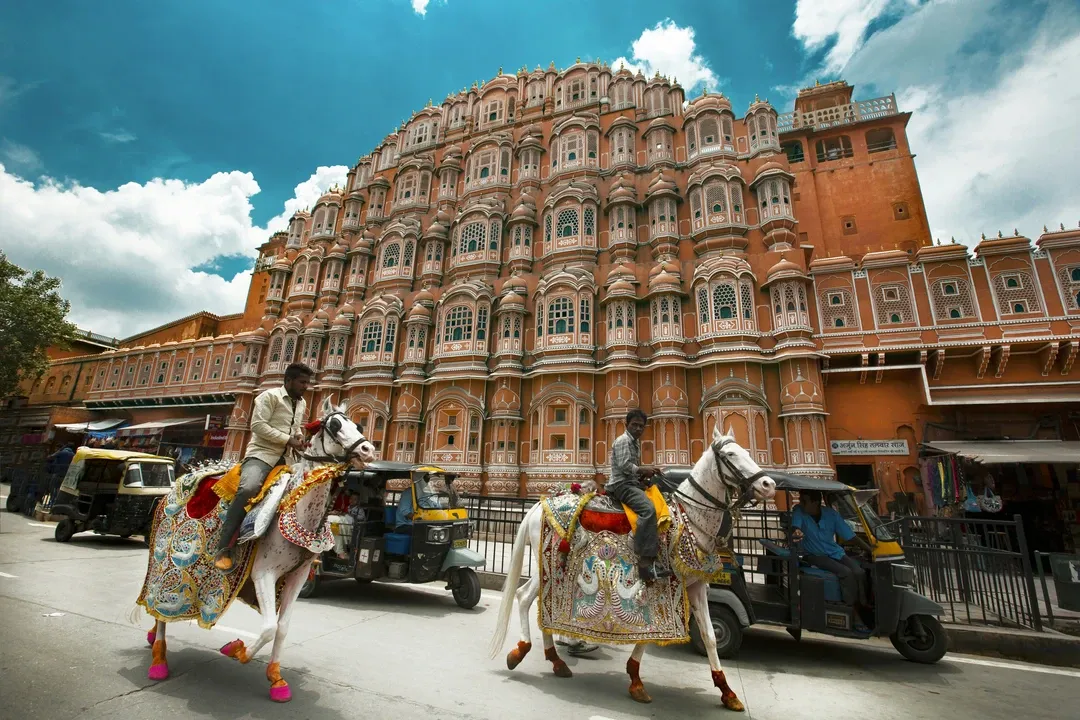 A dynamic street scene in Jaipur with traditionally decorated horses in front of the magnificent pink Hawa Mahal palace