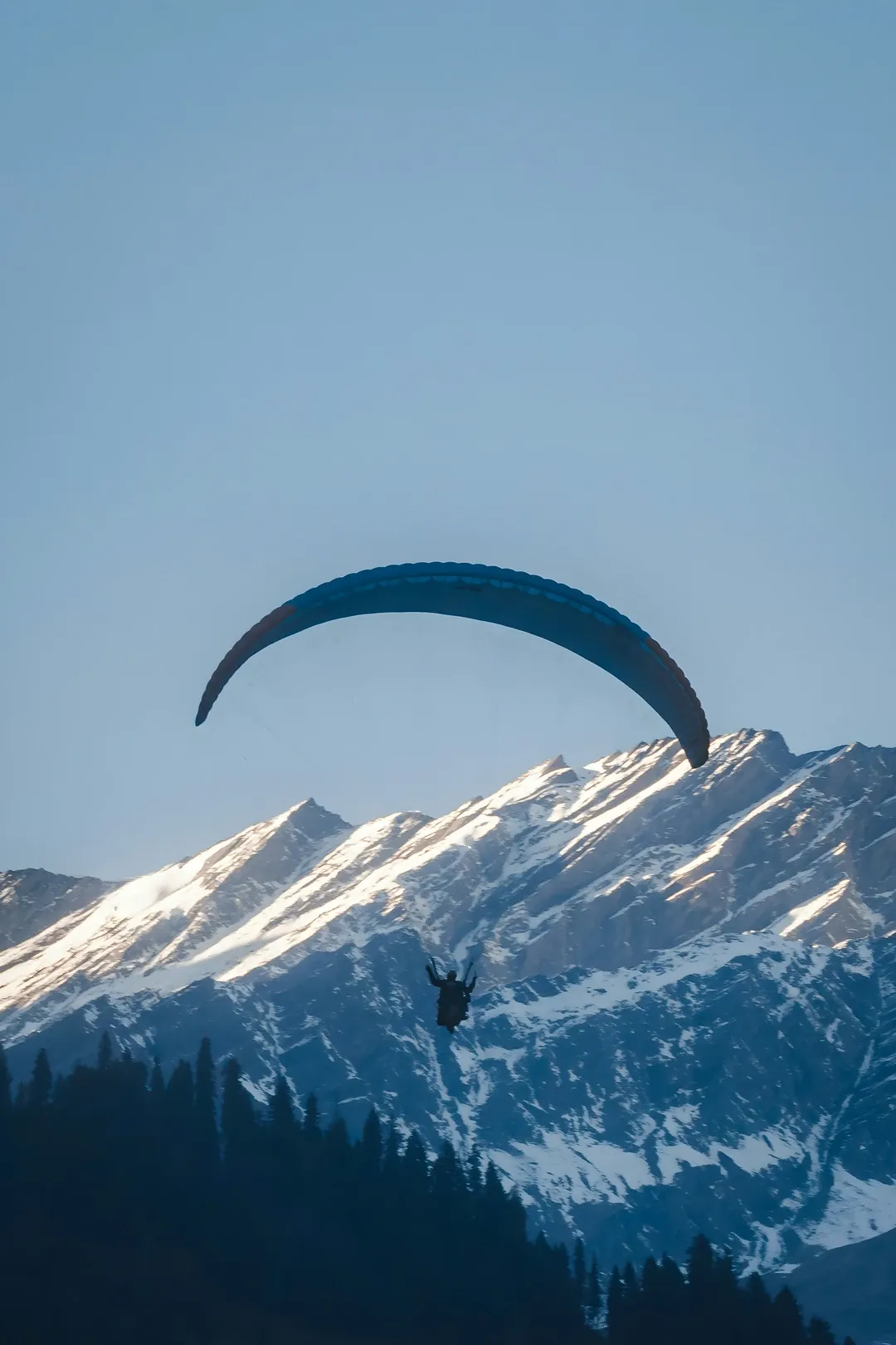 A person paragliding with a stunning view of the snow-capped Himalayan mountains in Manali.