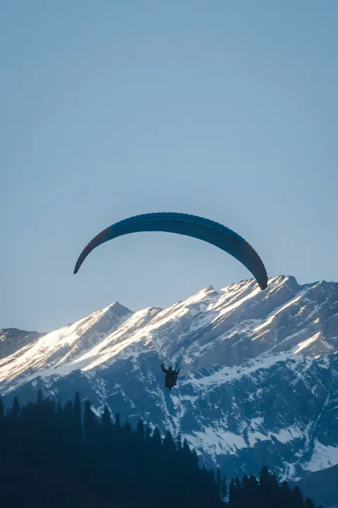 A person paragliding with a stunning view of the snow-capped Himalayan mountains in Manali.
