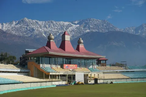 The iconic HPCA cricket stadium in Dharamshala, with its red pavilion set against the snow-capped Dhauladhar mountains.