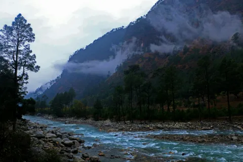  The turquoise waters of the Parvati River flow through a rocky valley, with mist clinging to the pine-covered mountains of Kasol