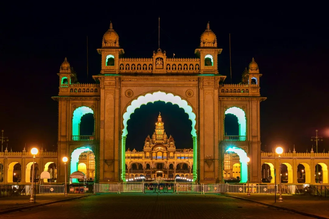 The magnificent Mysore Palace, illuminated with lights, is perfectly framed through the grand archway of its entrance gate at night