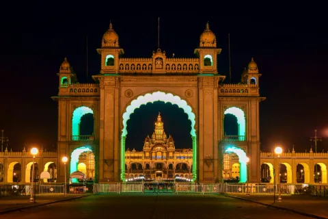 The magnificent Mysore Palace, illuminated with lights, is perfectly framed through the grand archway of its entrance gate at night