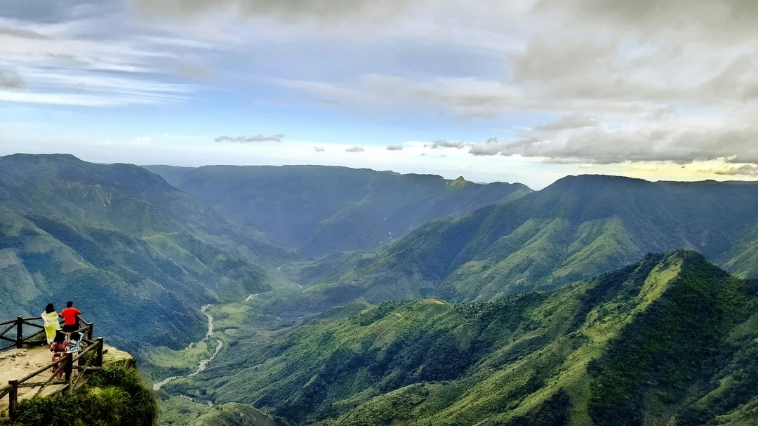 A panoramic view from a clifftop, looking out over the vast, deep green gorges and rolling hills of Laitlum Canyons in Meghalaya