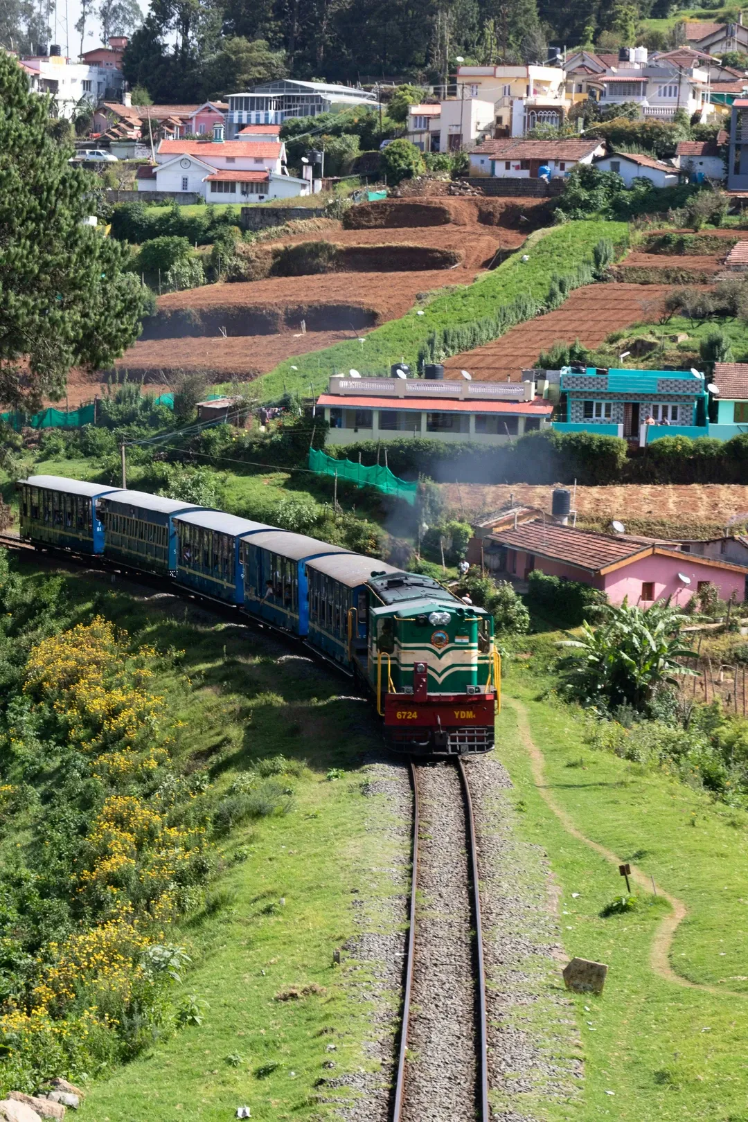 The famous Ooty toy train on its scenic journey through the lush green hills and terraced farms of the Nilgiris.