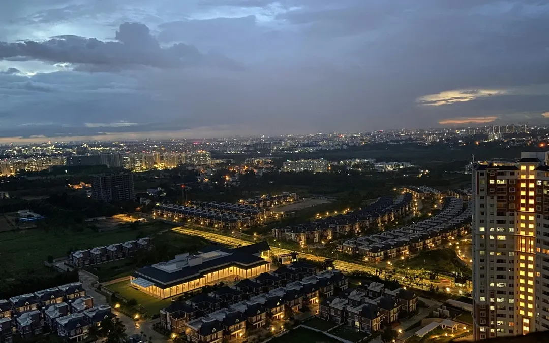 An aerial view of the Prestige Lakeside Habitat residential complex in Bengaluru at twilight, with city lights glowing