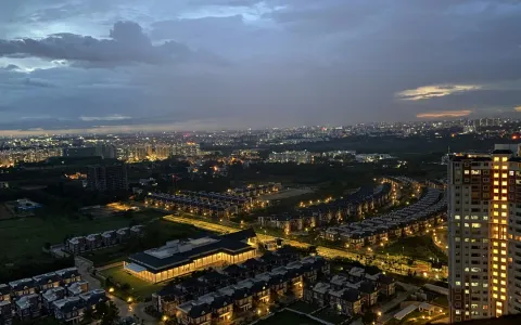 An aerial view of the Prestige Lakeside Habitat residential complex in Bengaluru at twilight, with city lights glowing